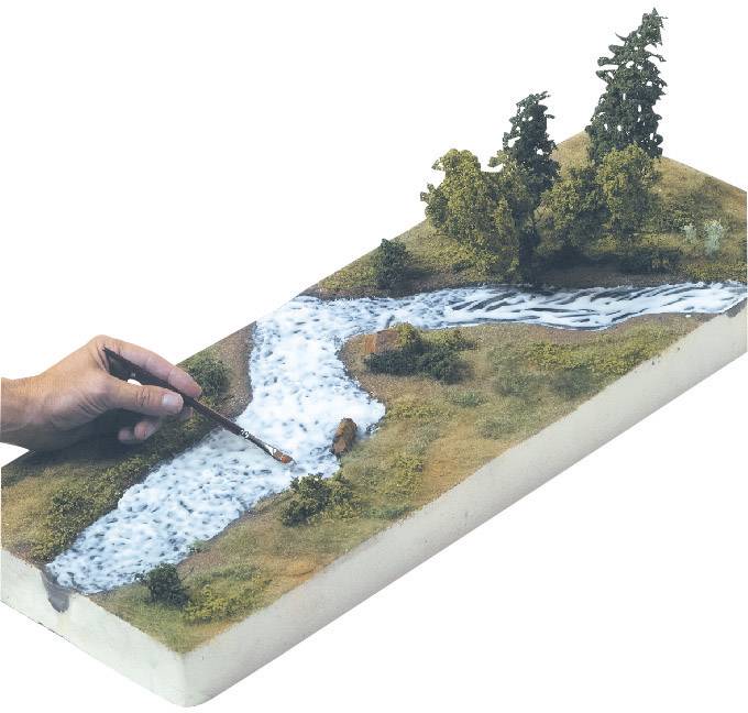 Eine Hand malt mit einem Pinsel einen Fluss auf ein Landschaftsdiorama mit Bäumen, das ein naturgetreues Modell einer Flusslandschaft darstellt.