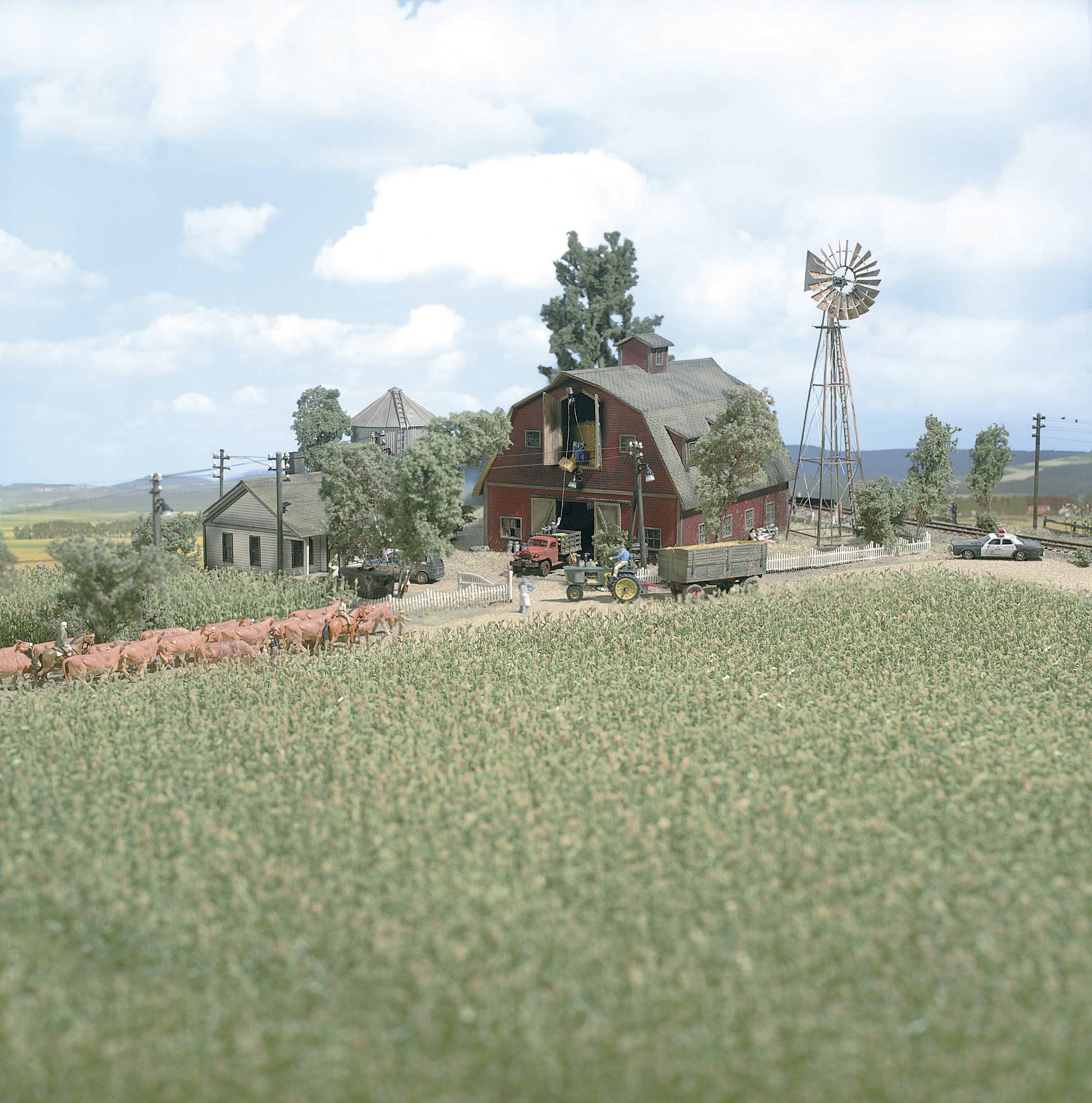 Eine ländliche Szene zeigt eine rote Scheune, Felder mit Getreide und Rinder, einen Windmühle-Turm und Bauernhäuser unter wolkigem Himmel.