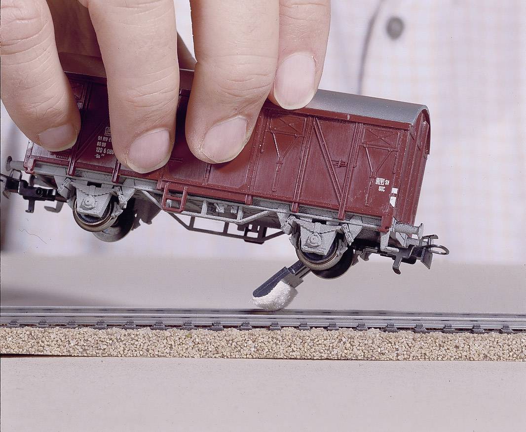 Ein Modellzugwaggon wird von einer Hand über ein Gleis gehalten, als ob er angehoben oder auf das Gleis gesetzt wird.