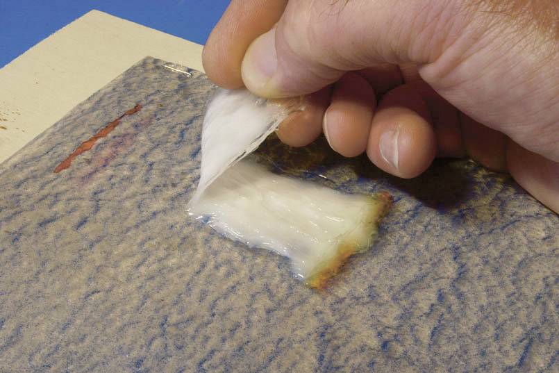 Eine Hand zieht eine durchsichtige Schicht von einer blauen Oberfläche ab, die Teil eines Reinigungs- oder Konservierungsprozesses sein könnte.