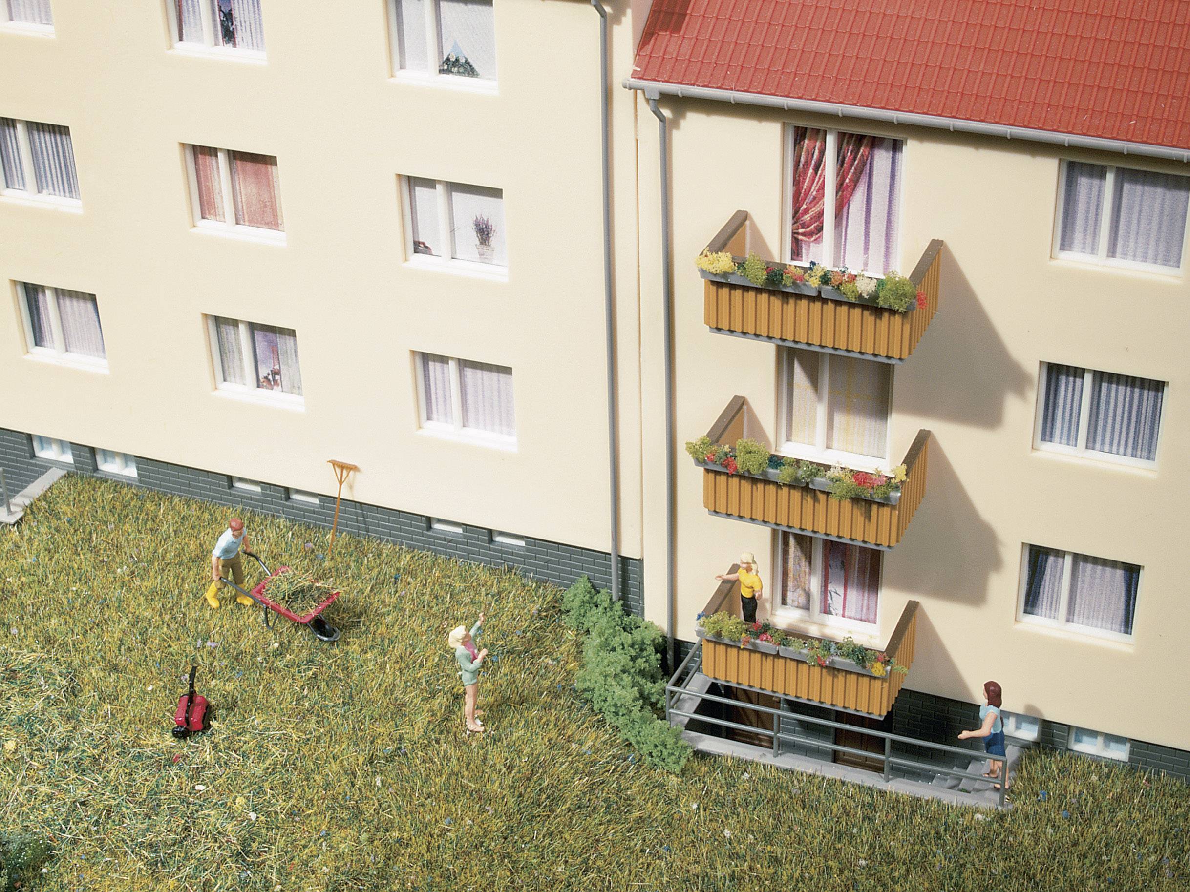 Mehrfamilienhaus mit Balkonen, Bewohner unterhalten sich und pflegen den Garten mit Rasenmäher und Rechen.