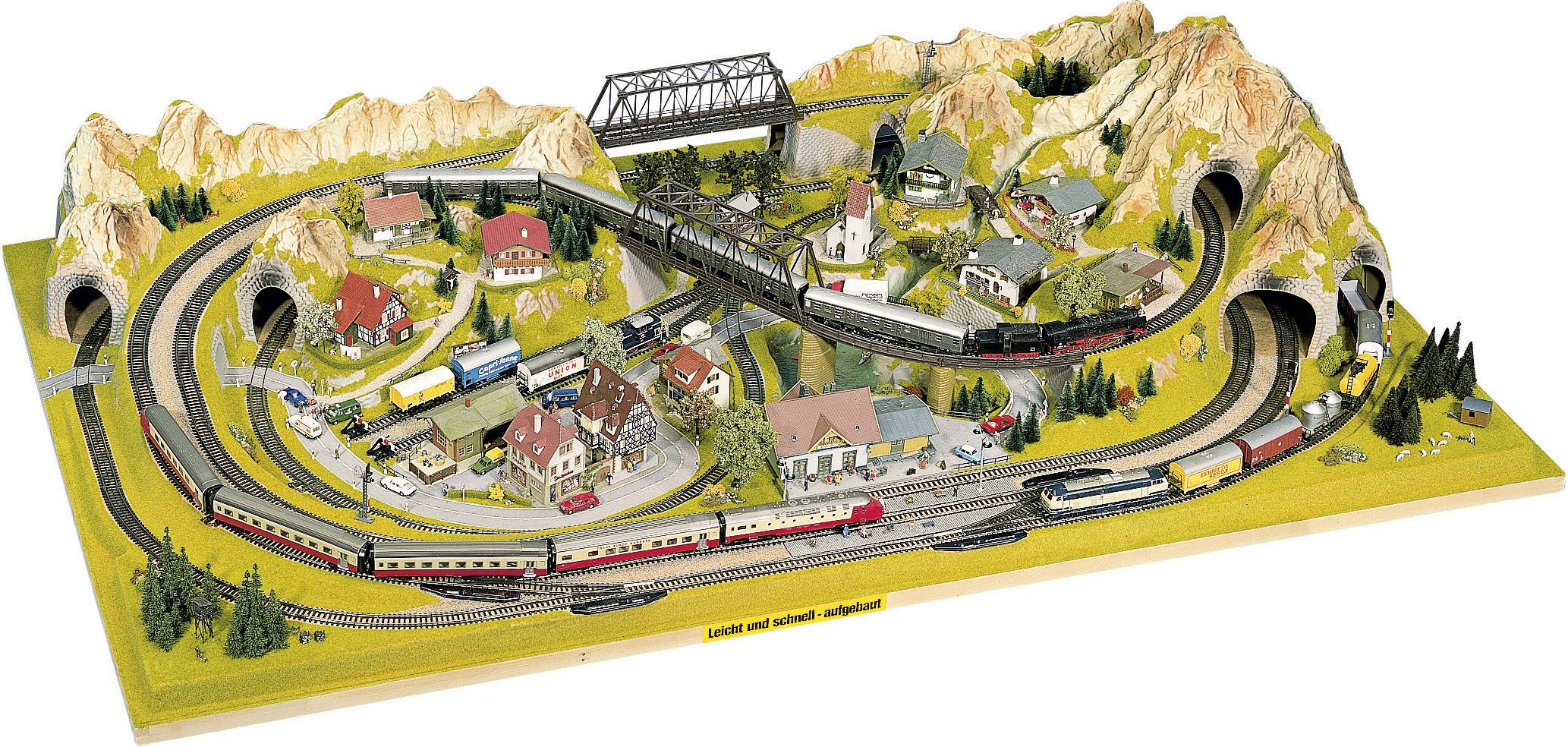 'Modelleisenbahn-Landschaft mit Bergen, mehreren Zügen, Tunneln und kleinen Dörfern.'