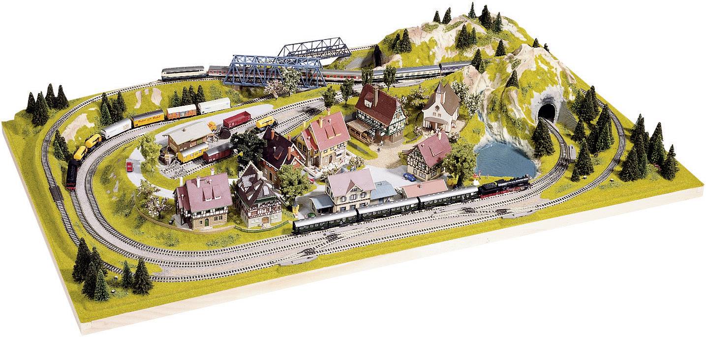 Modelleisenbahn-Diorama mit Zugstrecken durch eine Miniaturlandschaft. Häuser, Hügel, eine Brücke und Bäume sind sichtbar.