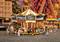 Ein Miniatur-Karussell in einem Freizeitpark-Diorama. Figuren stehen um das Karussell herum. Hintergrund zeigt ein Riesenrad.