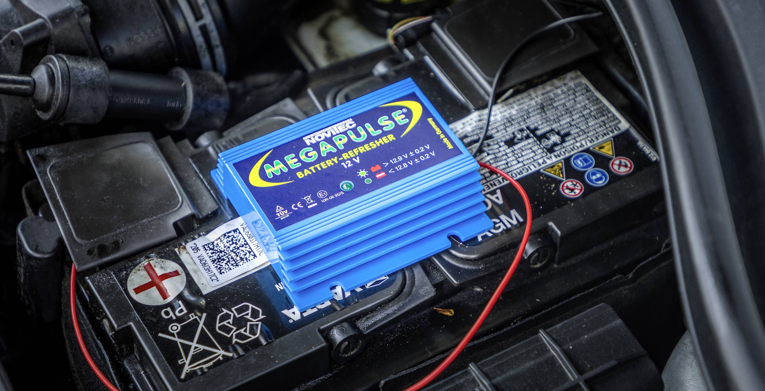 Ein blauer Batterieregenerator mit der Aufschrift 'Megapulse' ist auf einer Autobatterie angeschlossen, um ihre Lebensdauer zu verlängern.