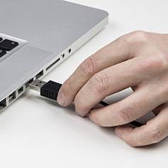 Eine Hand steckt einen USB-Stick in einen Laptop ein.