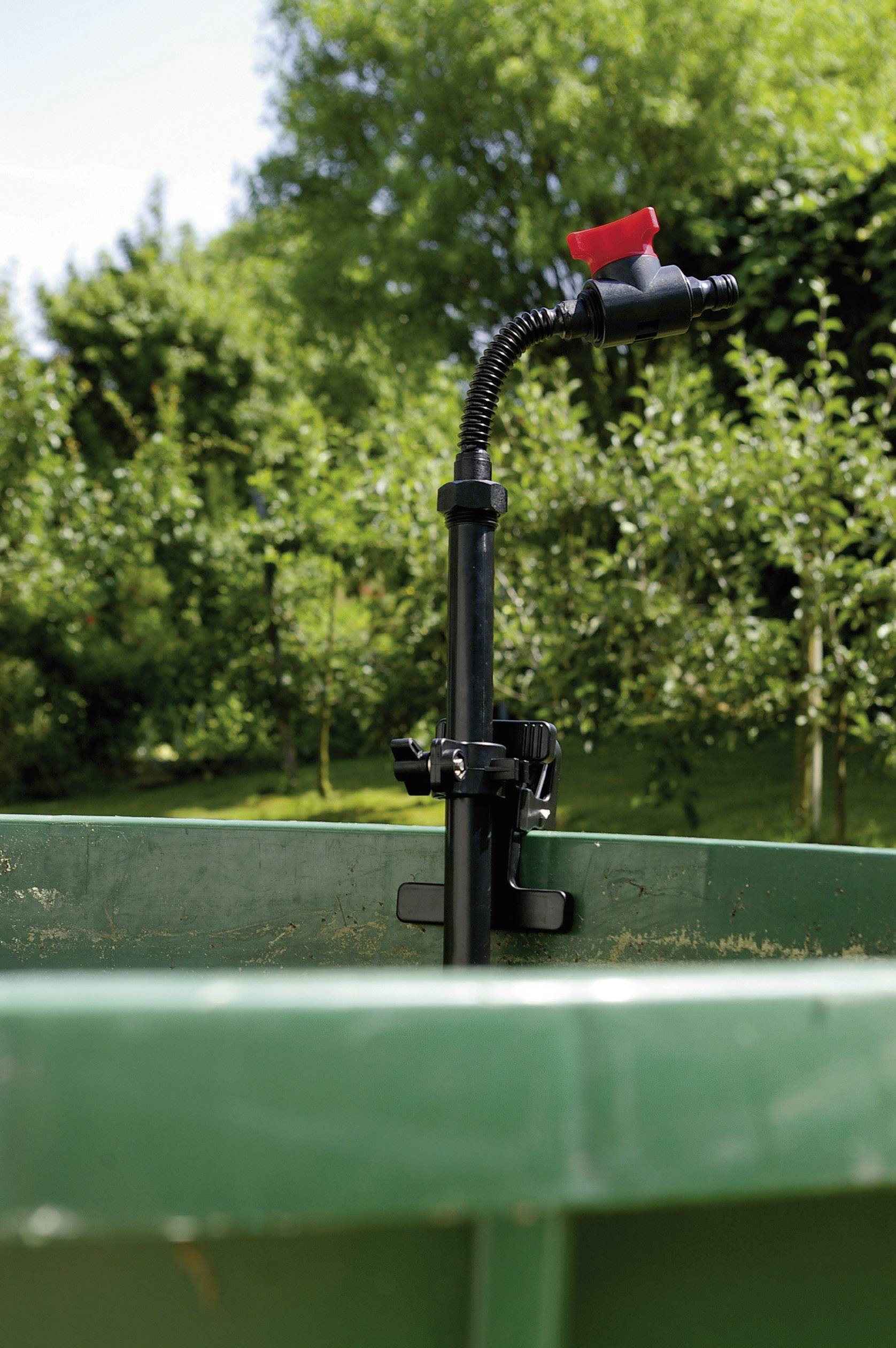 'Nahaufnahme eines Bewässerungssystems in einem grünen Wassertank im Freien. Im Hintergrund sind Bäume und Vegetation zu sehen.'
