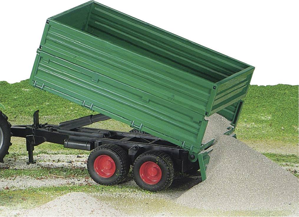 Ein grüner Anhänger mit roten Rädern kippt Sand auf den Boden in einer ländlichen Umgebung ab.