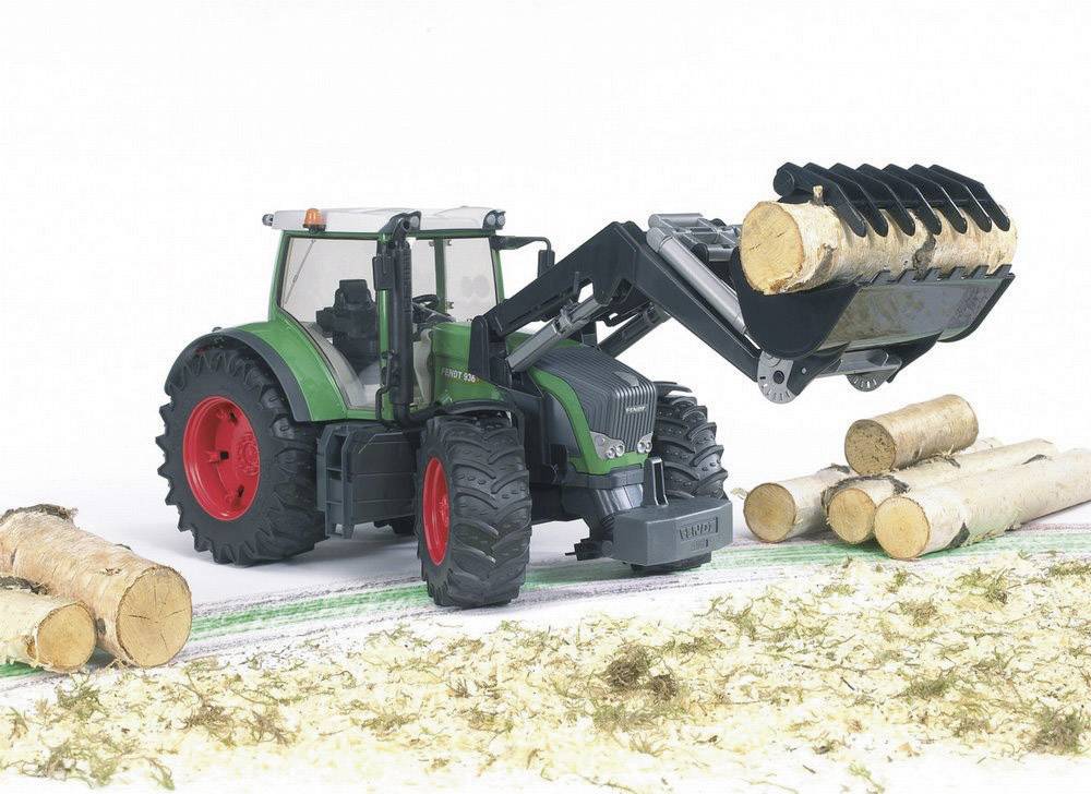 Ein grüner Traktor mit rotem Rad transportiert Holzstämme mit einem Frontlader. Der Boden ist mit Spänen bedeckt.