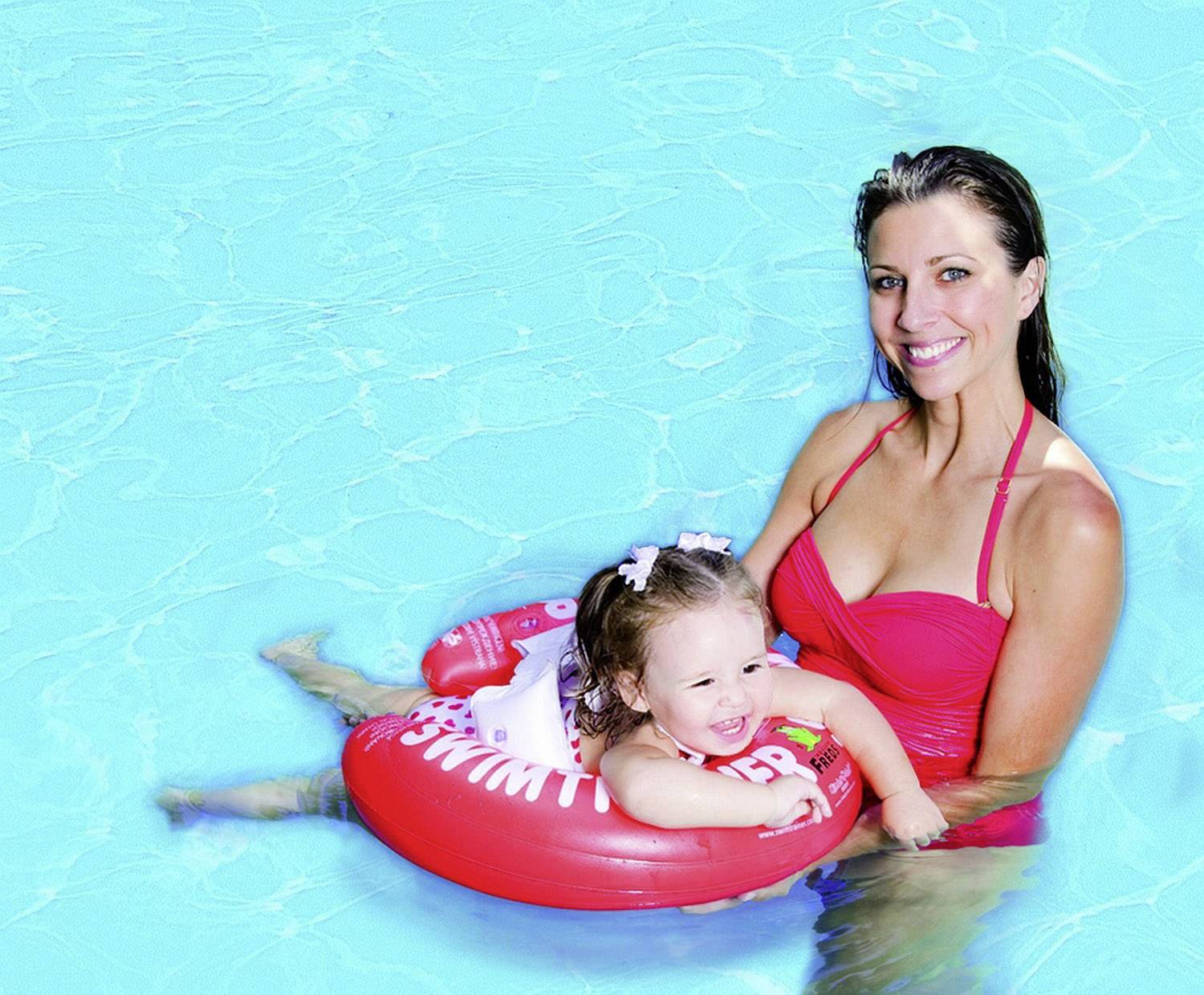 Eine Frau im roten Badeanzug hält ein lachendes Kleinkind im Schwimmring in einem Pool.