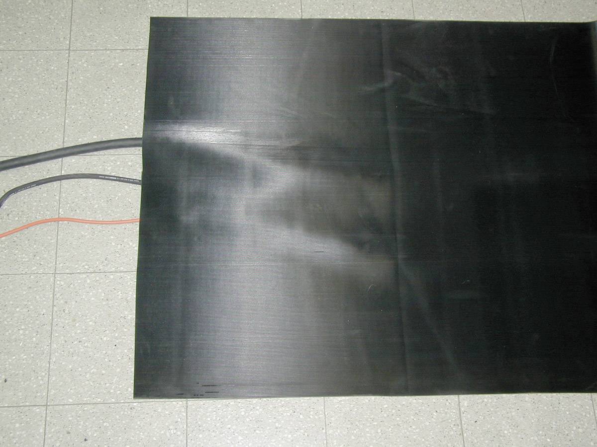 Ein rechteckiges schwarzes Blatt liegt auf einem grauen gefliesten Boden. Drei Kabel ragen aus der linken Seite heraus.