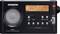 Ein schwarzes Radio mit digitalem Display zeigt die Frequenz 100.7 FM an. Links ist ein Lautsprecher, rechts Steuertasten.