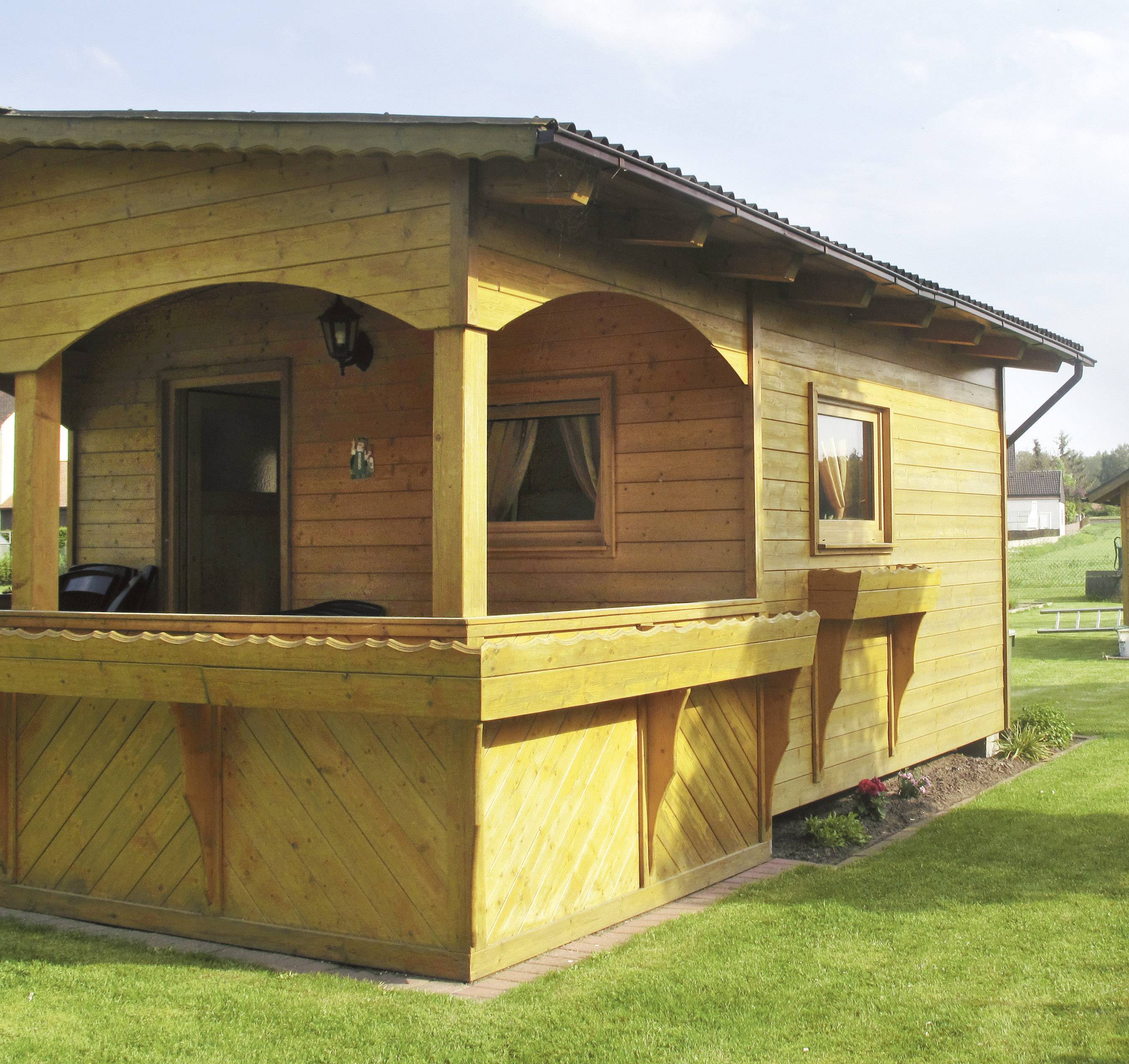 Kleines, gemütliches Holzhaus mit überdachter Veranda und Zierbalkon, umgeben von Rasen, bei sonnigem Wetter.