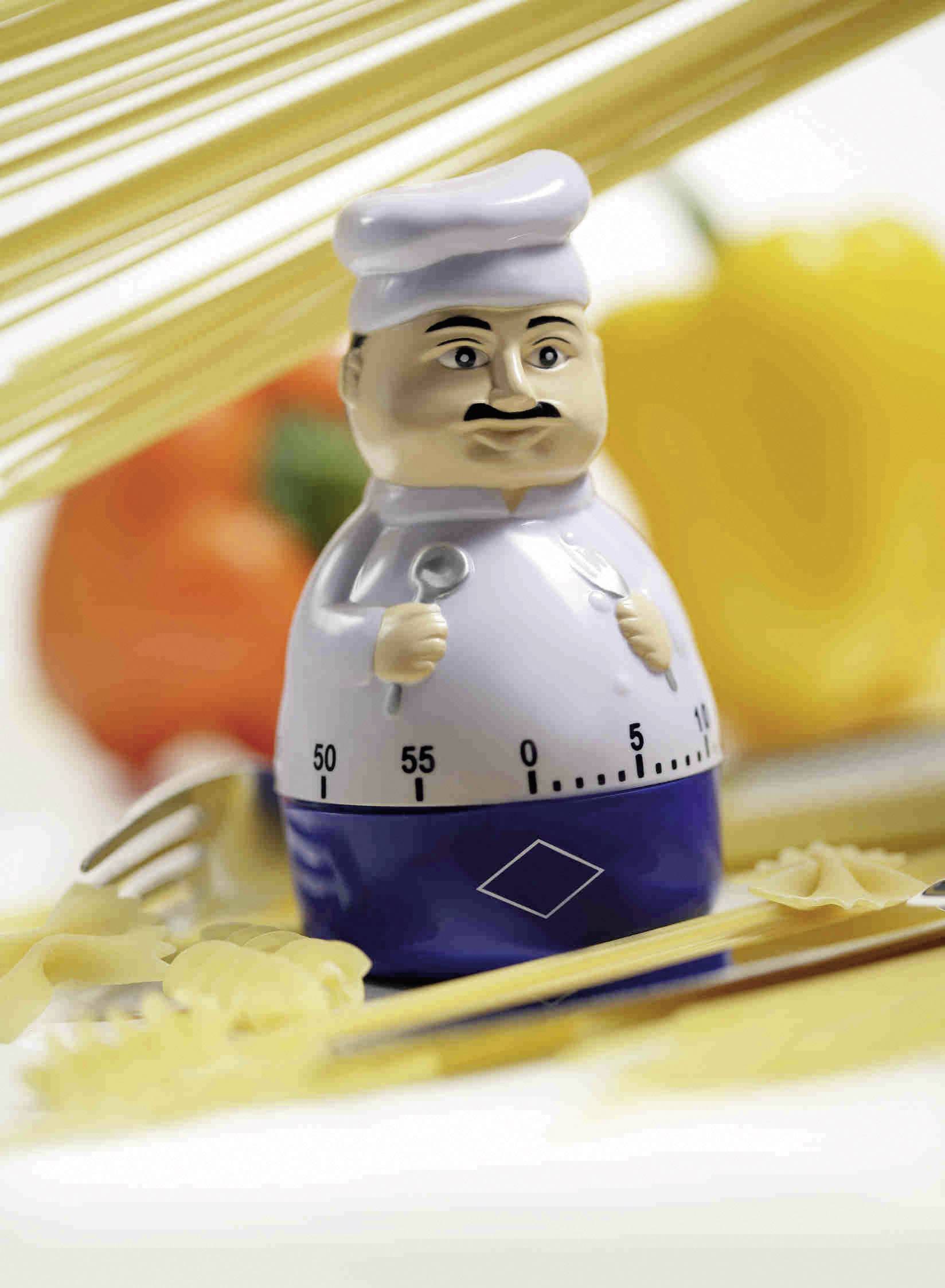 Ein Küchentimer in Form eines Kochs umgeben von Nudeln, einer Gabel und Paprika im Hintergrund.