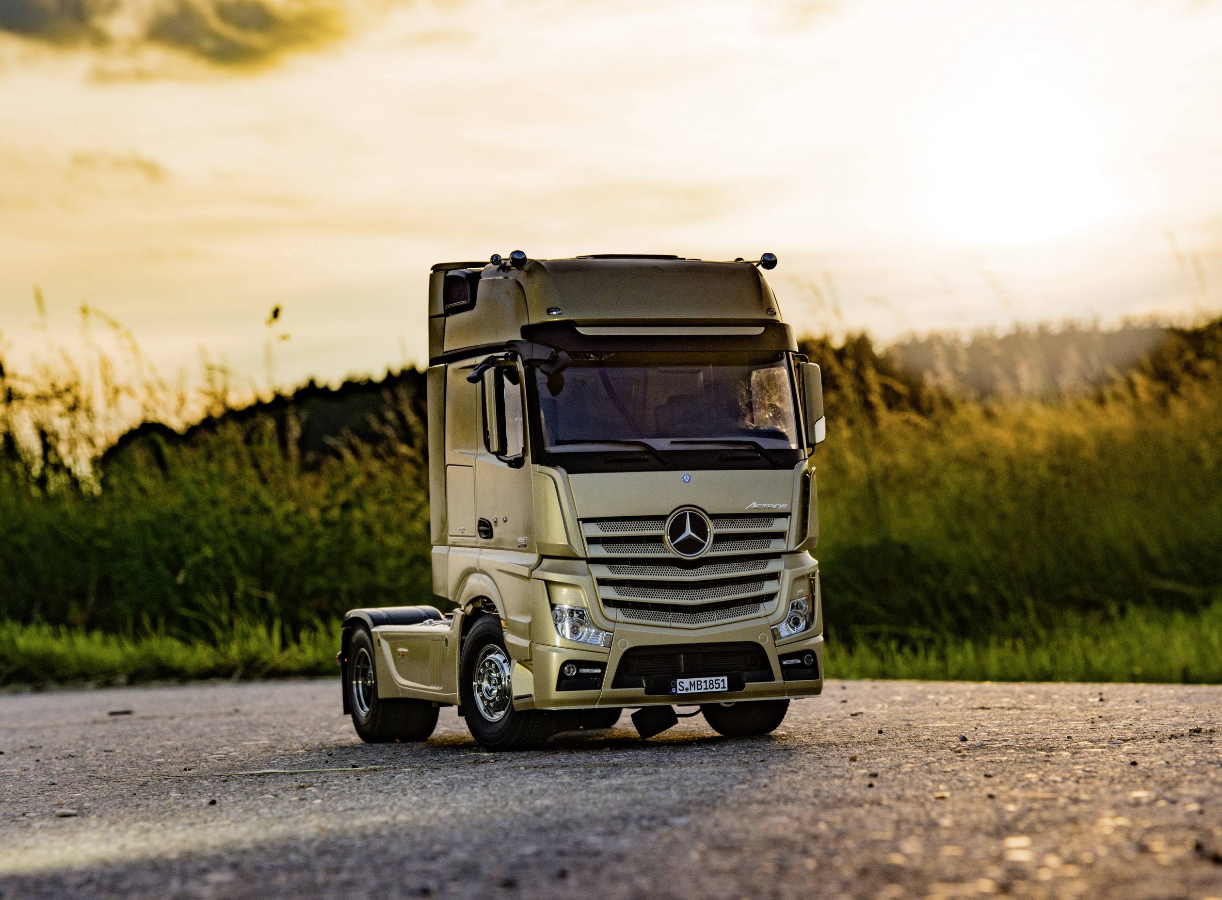 Ein Modell-Lkw steht auf einer Straße bei Sonnenuntergang. Grüne Wiesen im Hintergrund und ein goldener Himmel darüber.