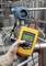 Eine Person misst mit einem gelben digitalen Multimeter den Druck eines blauen industriellen Drucksensors, umgeben von Metallrohren.