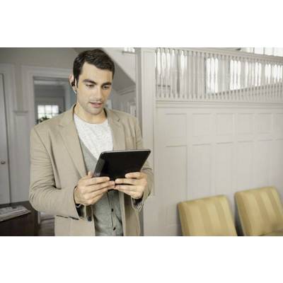 Mann in beigem Blazer nutzt ein Tablet in modernem Büro, trägt Bluetooth-Headset. Im Hintergrund sind helle Wände und Stühle.