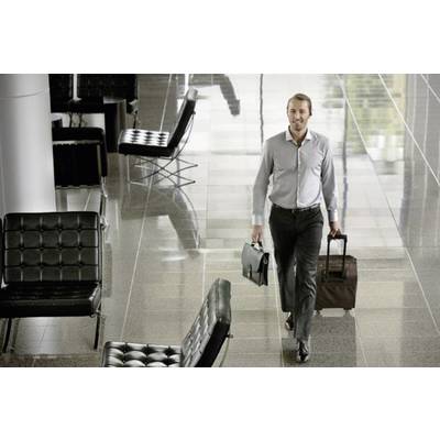 Ein Mann in Geschäftsanzug geht durch einen modernen Flughafen, trägt eine Aktentasche in der einen und einen Rollkoffer in der anderen Hand.