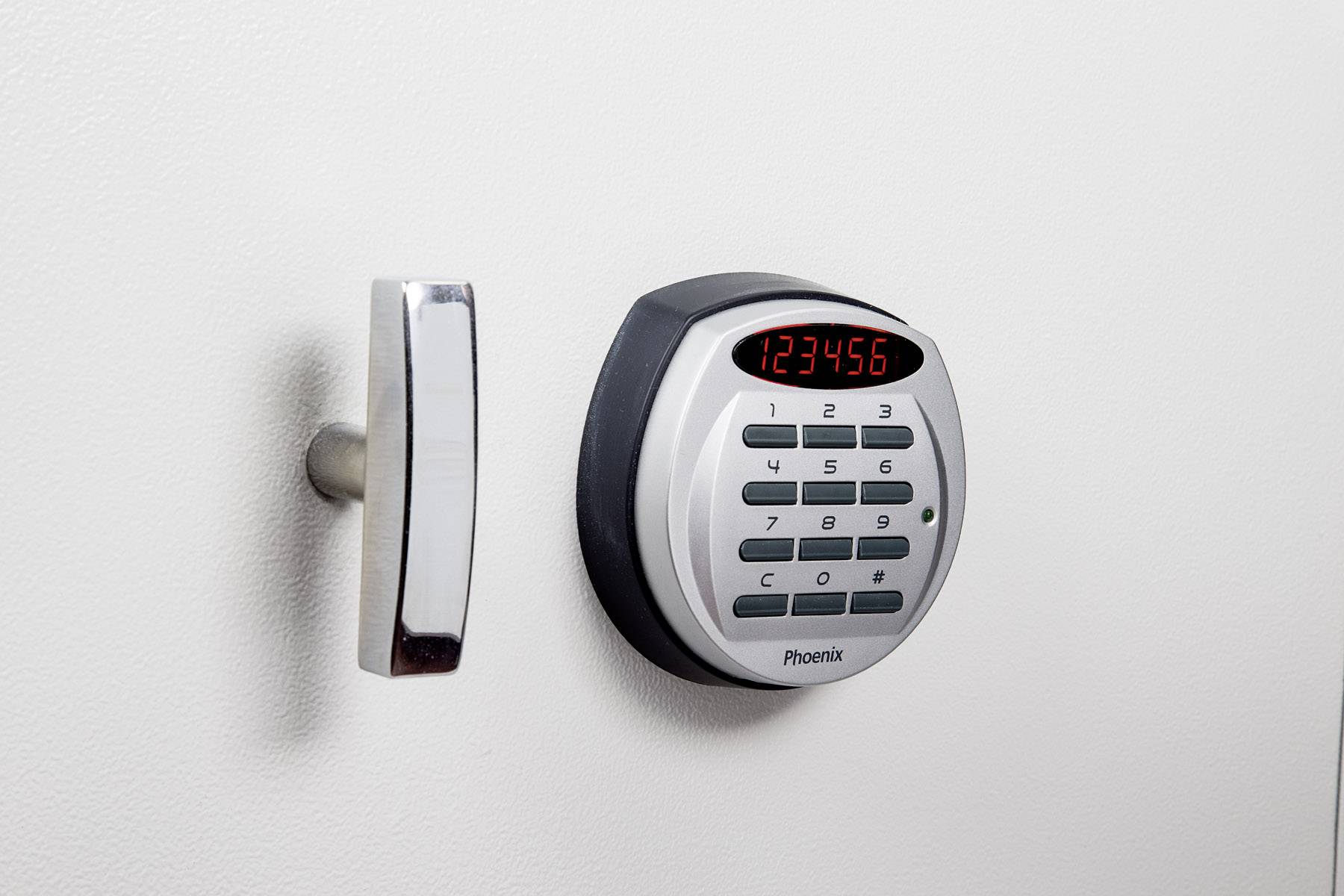 Ein elektronisches Zahlenschloss mit angezeigtem Code '123456' neben einem silbernen Griff auf einer weißen Oberfläche.