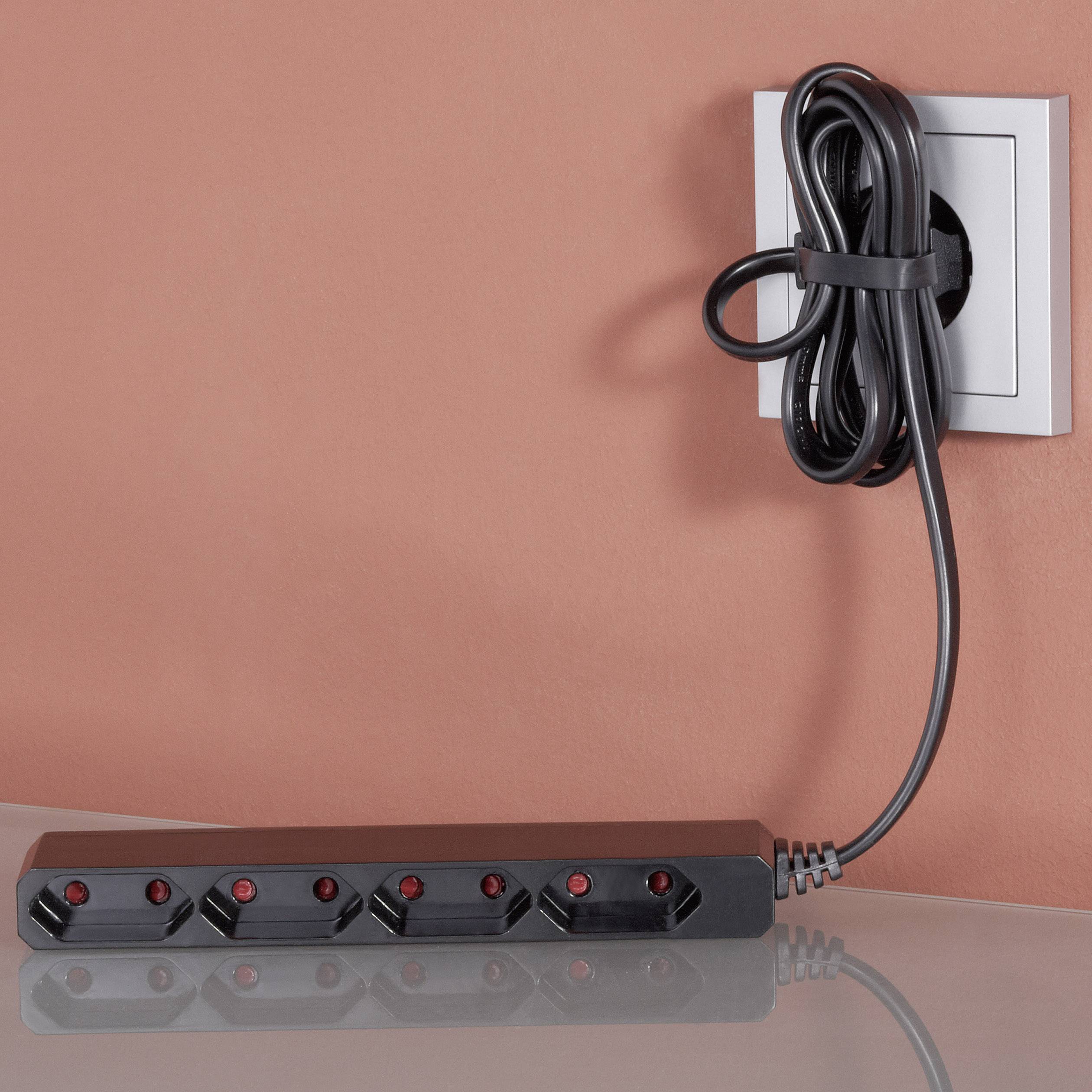 Eine leere, schwarze Steckdosenleiste liegt auf einem Tisch. Ein Netzkabel ist ordentlich aufgerollt und in eine Wandsteckdose eingesteckt.