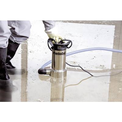 Eine Person bedient eine Tauchpumpe zum Abpumpen von Wasser auf einer überfluteten Betonfläche. Die Pumpe ist mit einem blauen Schlauch verbunden.