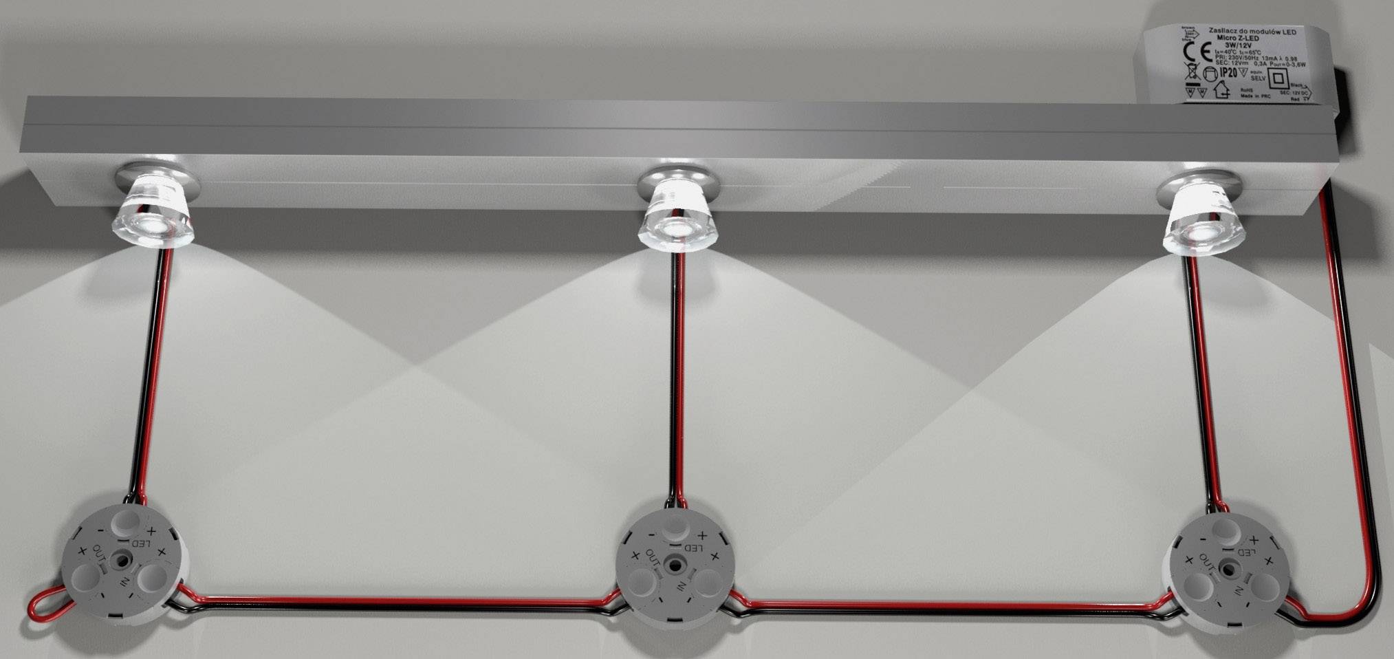 Drei Strahler an einer Leiste, leuchtend auf die darunterliegende Fläche. Kabel sind sichtbar, Details der Verkabelung gezeigt.