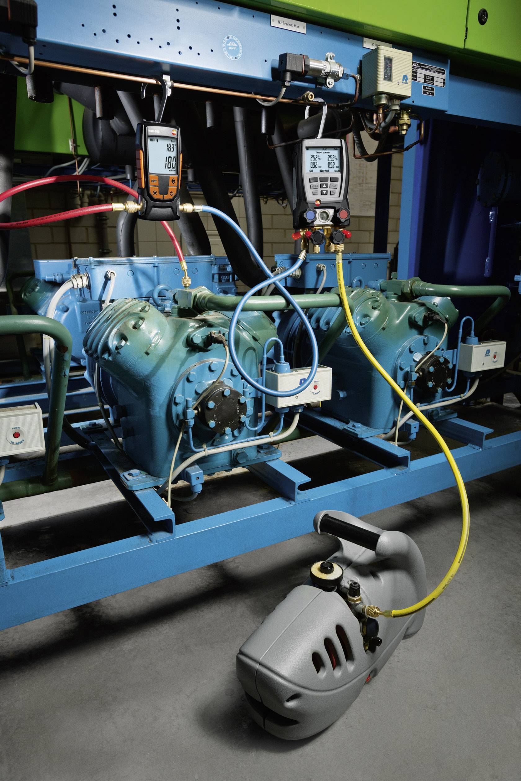 Industrielle Kühlsystemanlage mit zwei Kompressoren. Diagnosetools messen Betriebswerte. Umgebung wirkt technisch und funktional.