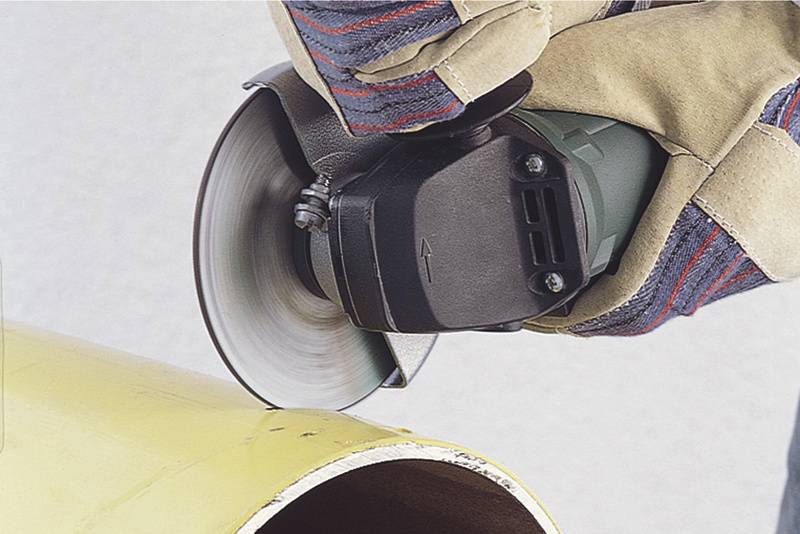 Eine Person schneidet mit einer elektrischen Winkelschleifmaschine ein gelbes Rohr. Schutzkleidung wird getragen.