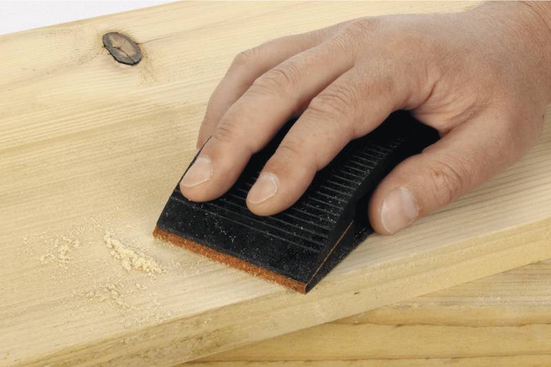Hand schleift mit einem Schleifblock ein Holzbrett.