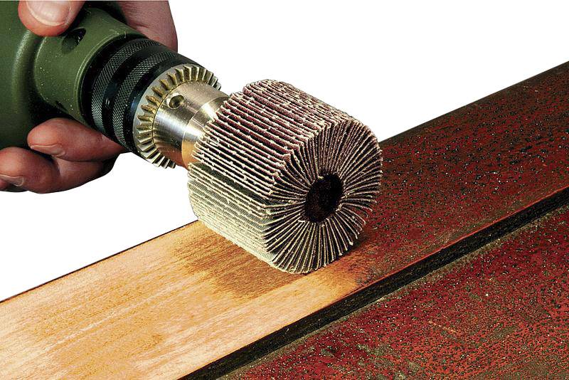 Eine Hand hält eine elektrische Bohrmaschine mit einem Schleifaufsatz, der eine Metalloberfläche poliert.