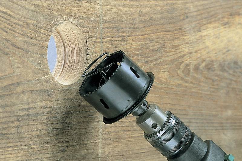 Ein Bohrer bearbeitet ein Holzbrett, während er ein rundes Loch schneidet.