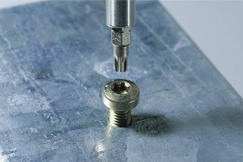 Ein Schraubenzieherkopf nähert sich einer Metall-Torx-Schraube auf einer ebenen Oberfläche.