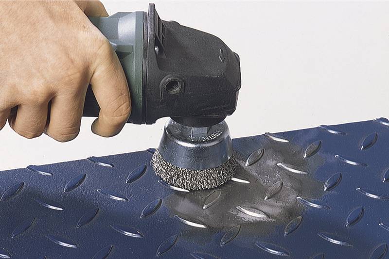 Eine Hand hält eine Schleifmaschine und poliert eine blaue Metalloberfläche, die bereits teilweise gesäubert ist.