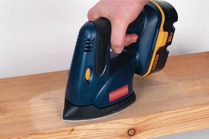 Eine Hand hält ein blaues Elektrogerät, das über ein Holzbrett gleitet. Es handelt sich vermutlich um eine kabellose Schleifmaschine.