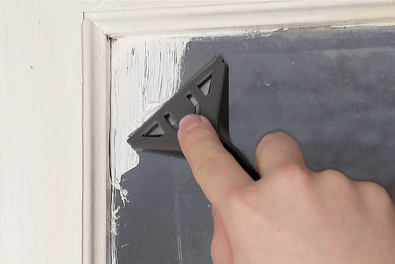 Eine Hand entfernt mit einem Schaber weiße Farbe vom Rand eines Fensters.