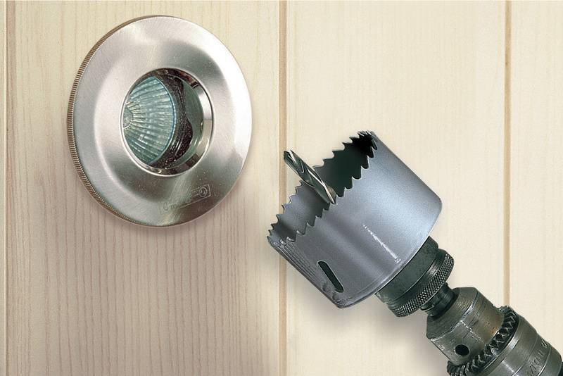 Bohrkrone neben einem runden Lüftungsgitter, das in eine Holzwand eingebaut ist, zeigt den Installationsprozess.