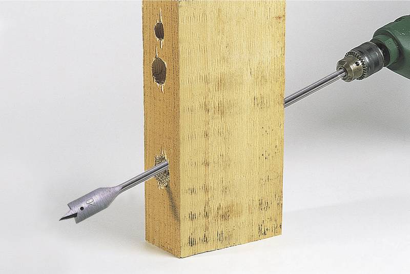 Ein Holzbohrer bohrt ein rechteckiges Holzstück. Der Bohrer hat bereits Löcher in verschiedenen Größen in das Holz gemacht.