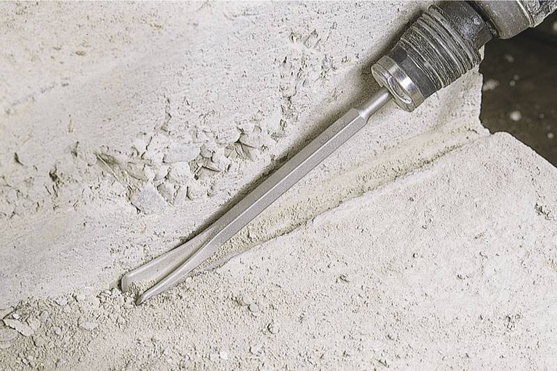Ein Pneumatikhammer meißelt Beton, wodurch eine Kante bearbeitet wird. Staub und Bruchstücke sind um die bearbeitete Stelle sichtbar.