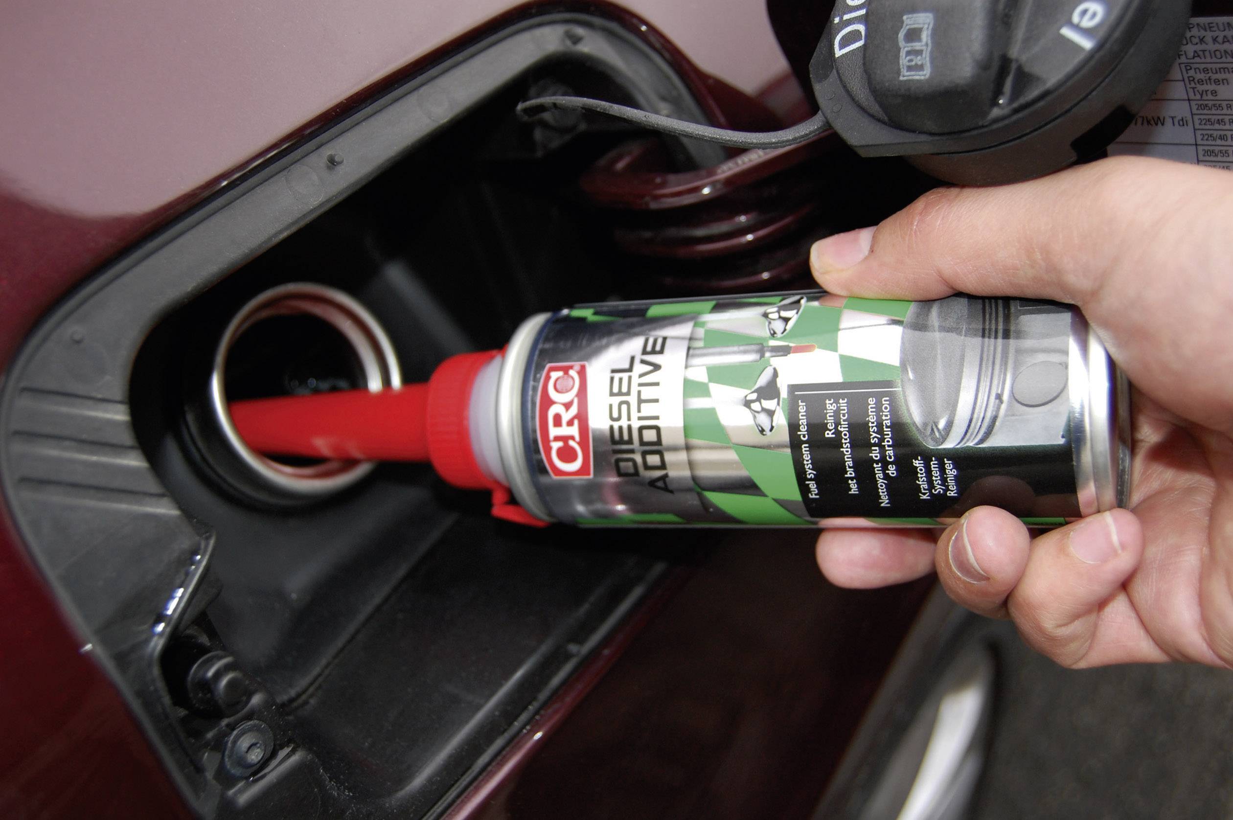 Hand hält Diesel-Additivflasche in der Nähe des Tankstutzens eines Autos, bereit zur Befüllung. Flasche zeigt Marke 'CRC'.