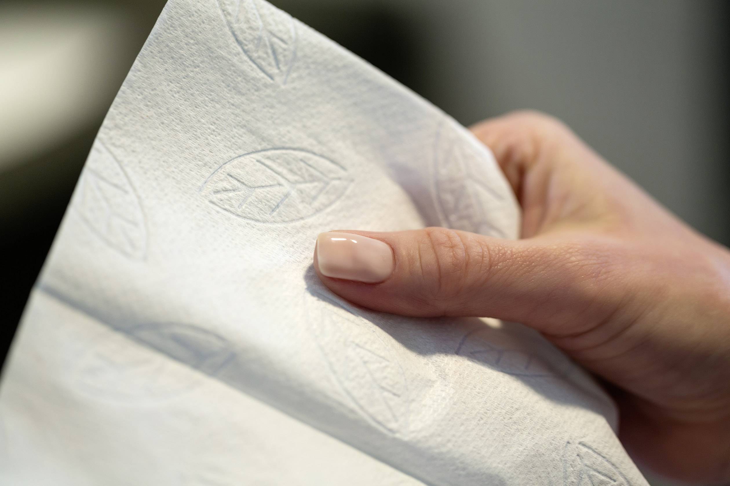 Eine Hand hält eine weiße Serviette mit eingeprägtem Blattmuster.