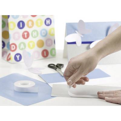 Eine Hand bastelt mit Papier und Klebeband auf einem Tisch. Im Hintergrund ist eine bunte Geburtstagskarte und Schmetterlingsdekorationen sichtbar.
