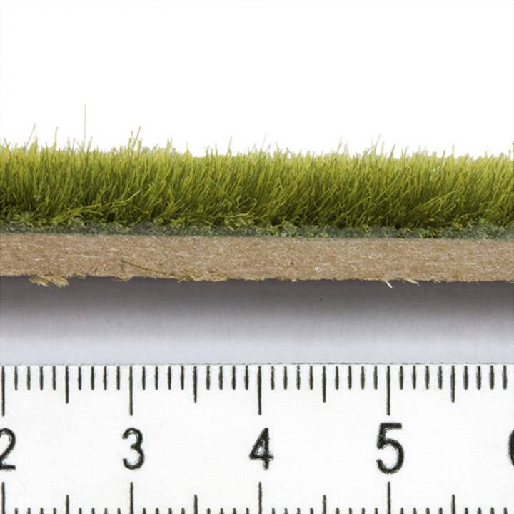 Nahaufnahme von künstlichem Rasen auf einem Holzbrett, das mit einem Lineal gemessen wird. Der Rasen ist etwa 2,5 Zentimeter hoch.