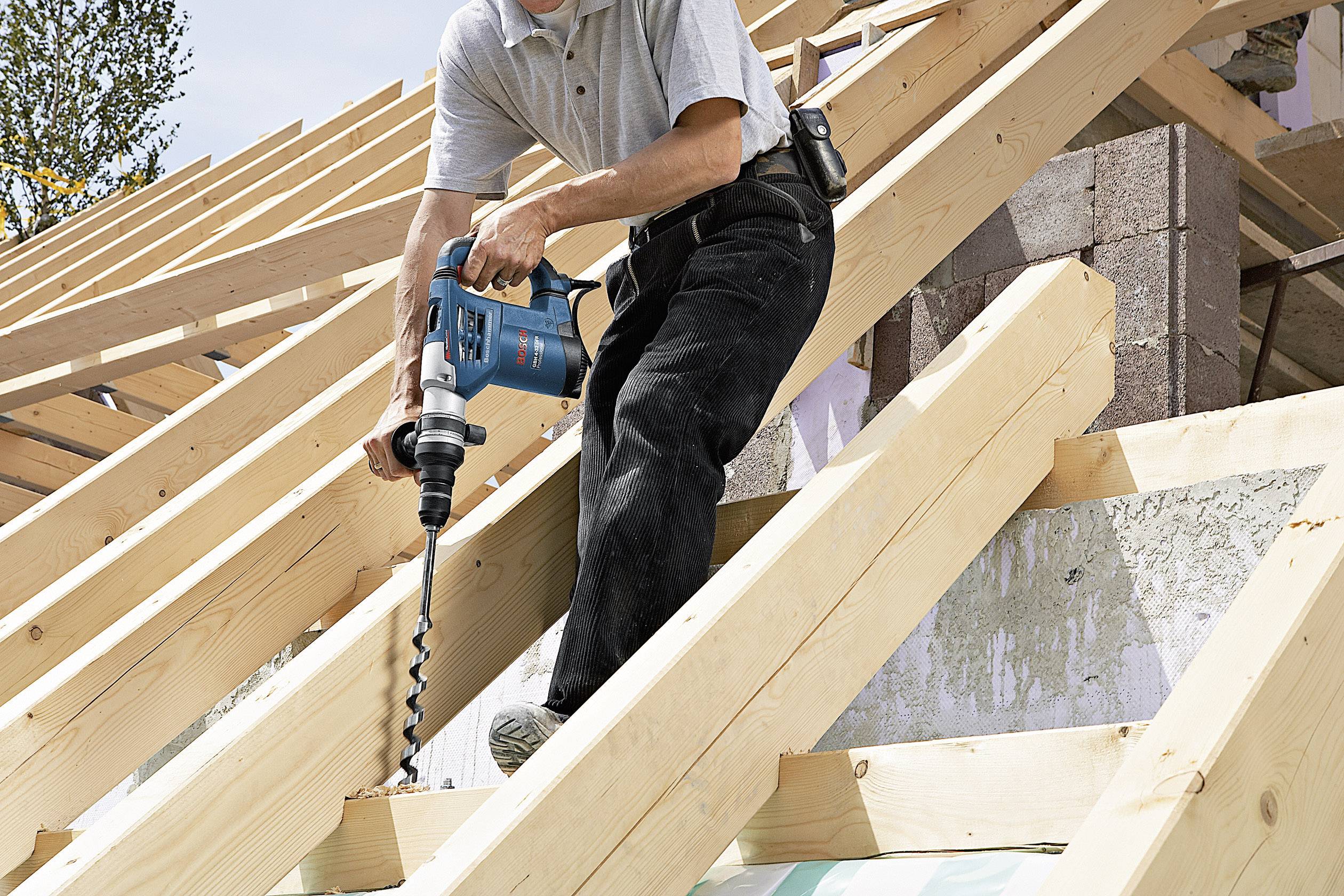 Eine Person benutzt ein Elektrobohrgerät, um Löcher in einen hölzernen Dachstuhl zu bohren. Baustelle im Freien.