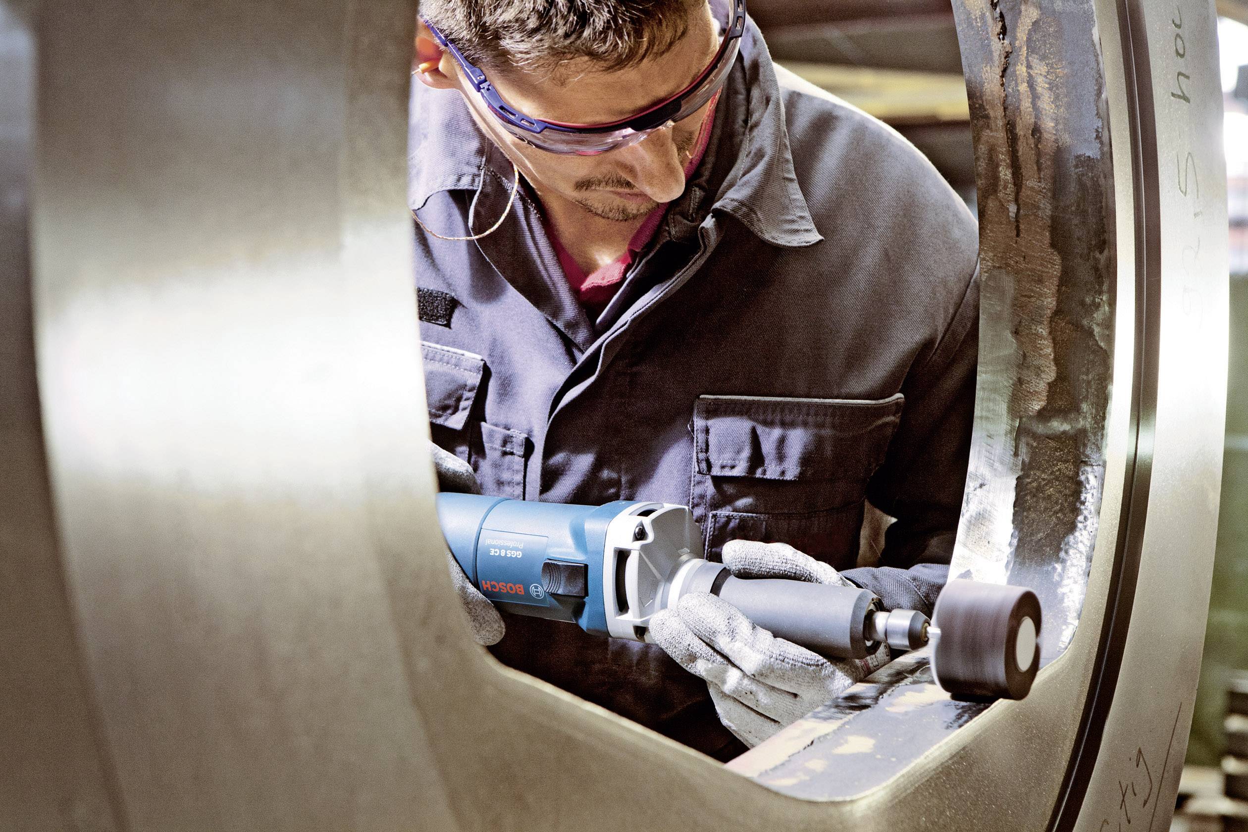 Ein Mann mit Schutzbrille schleift präzise die Innenfläche eines großen Metallrohrs, wobei er ein Elektrowerkzeug verwendet.
