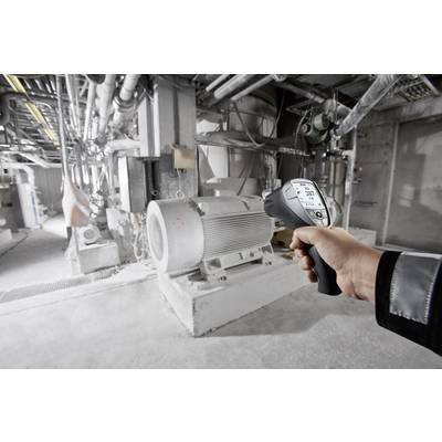 Eine Person misst die Temperatur eines großen Industriemotors mit einem Infrarot-Thermometer. Der Raum ist maschinell voll ausgestattet.