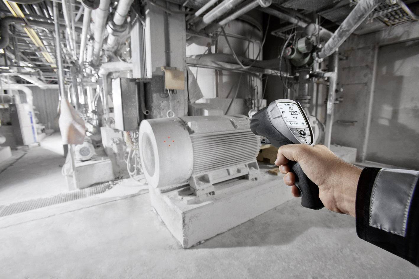 Person hält ein Infrarot-Temperaturmessgerät und misst die Temperatur einer großen Maschine in einer industriellen Anlage.