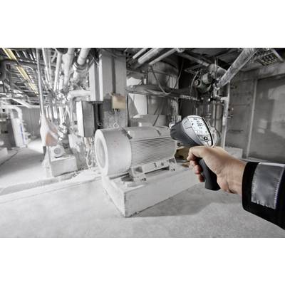 Person hält ein Infrarot-Temperaturmessgerät und misst die Temperatur einer großen Maschine in einer industriellen Anlage.