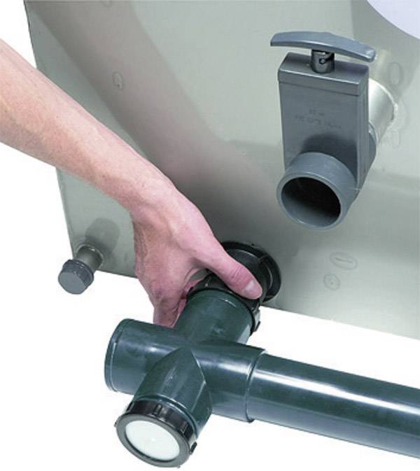 Eine Hand dreht einen Wasserhahn an einem grünen Rohrsystem, das an einem grauen Behälter angebracht ist.