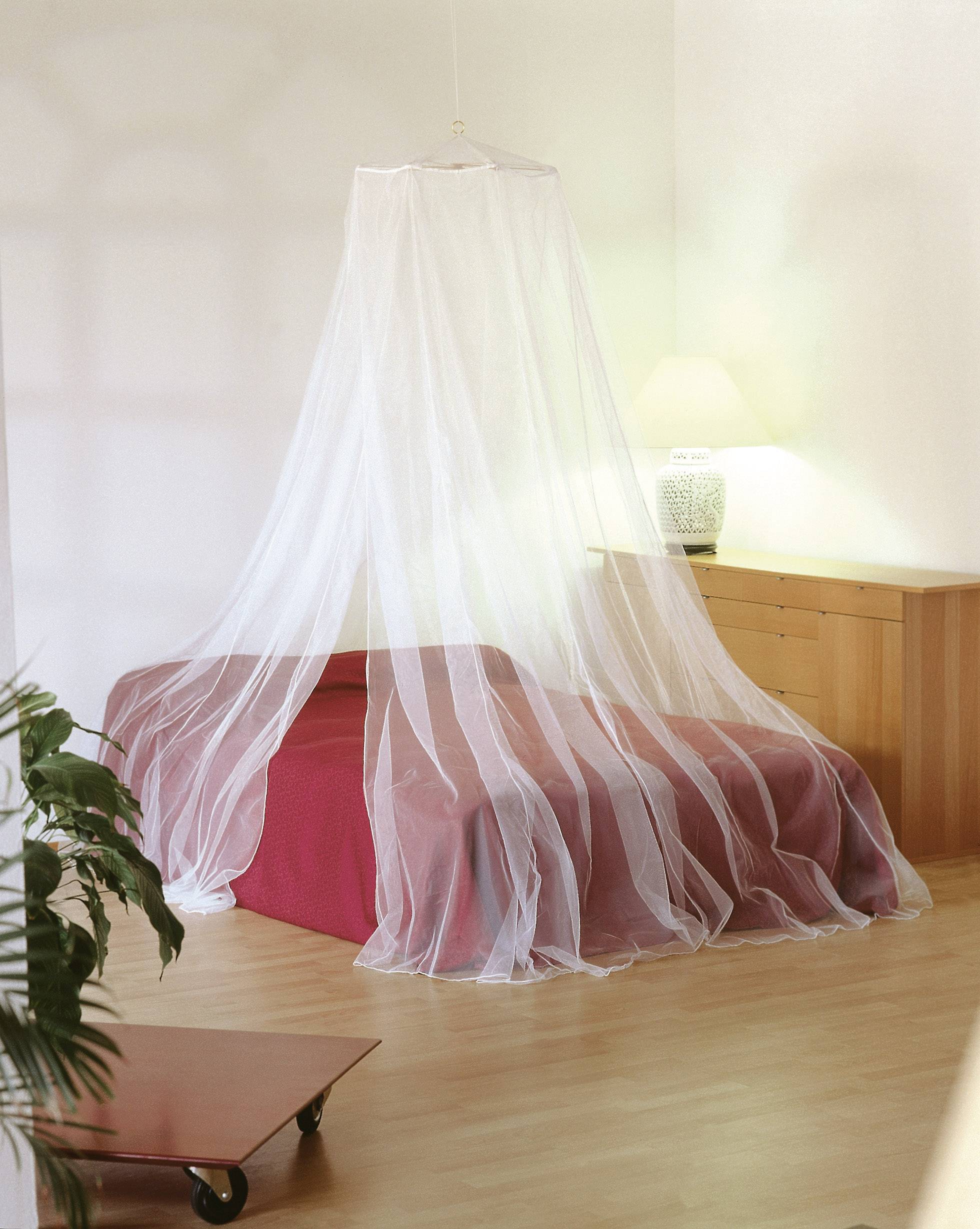 Ein Schlafzimmer mit Bett, bedeckt von einem transparenten Moskitonetz, daneben ein Nachttisch mit einer beleuchteten Lampe.