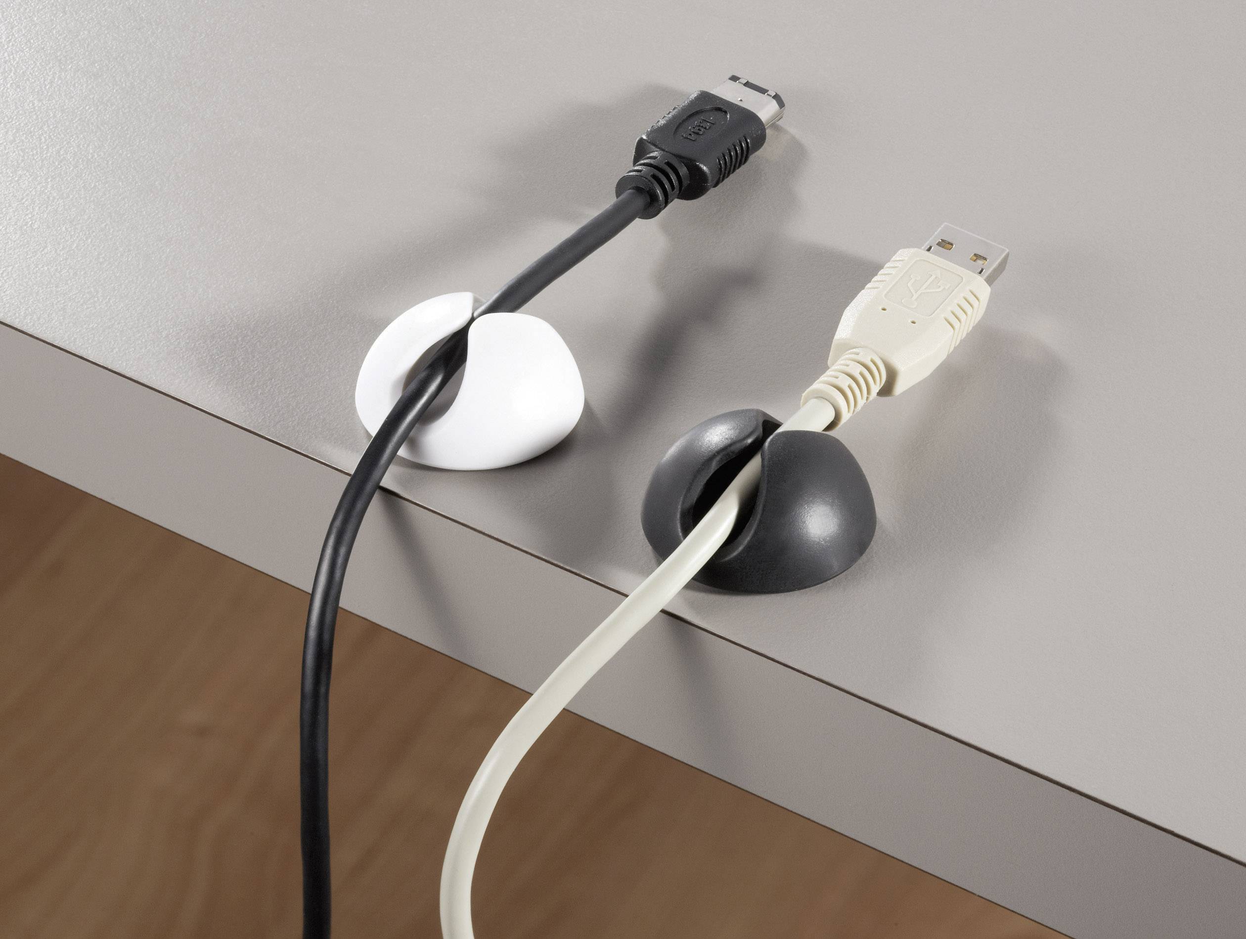Zwei Kabel, gehalten von schwarzen und weißen Kabelhaltern, die am Rand eines grauen Tischs platziert sind.